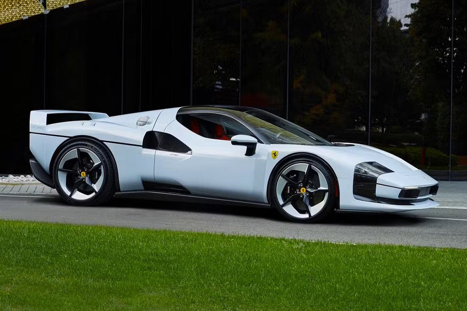 Moderné športové auto Ferrari v bielej farbe parkuje na trávniku pred elegantnou budovou.