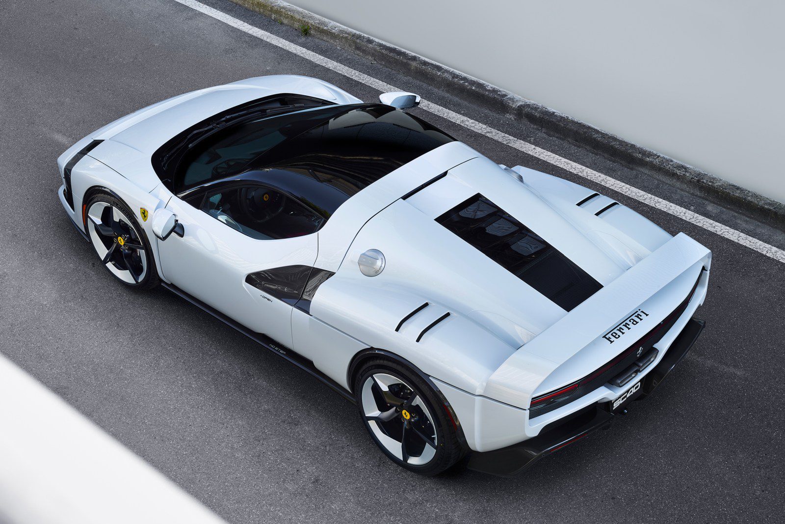 Biele športové auto Ferrari z vtáčej perspektívy na parkovisku; moderný dizajn a aerodynamické línie.