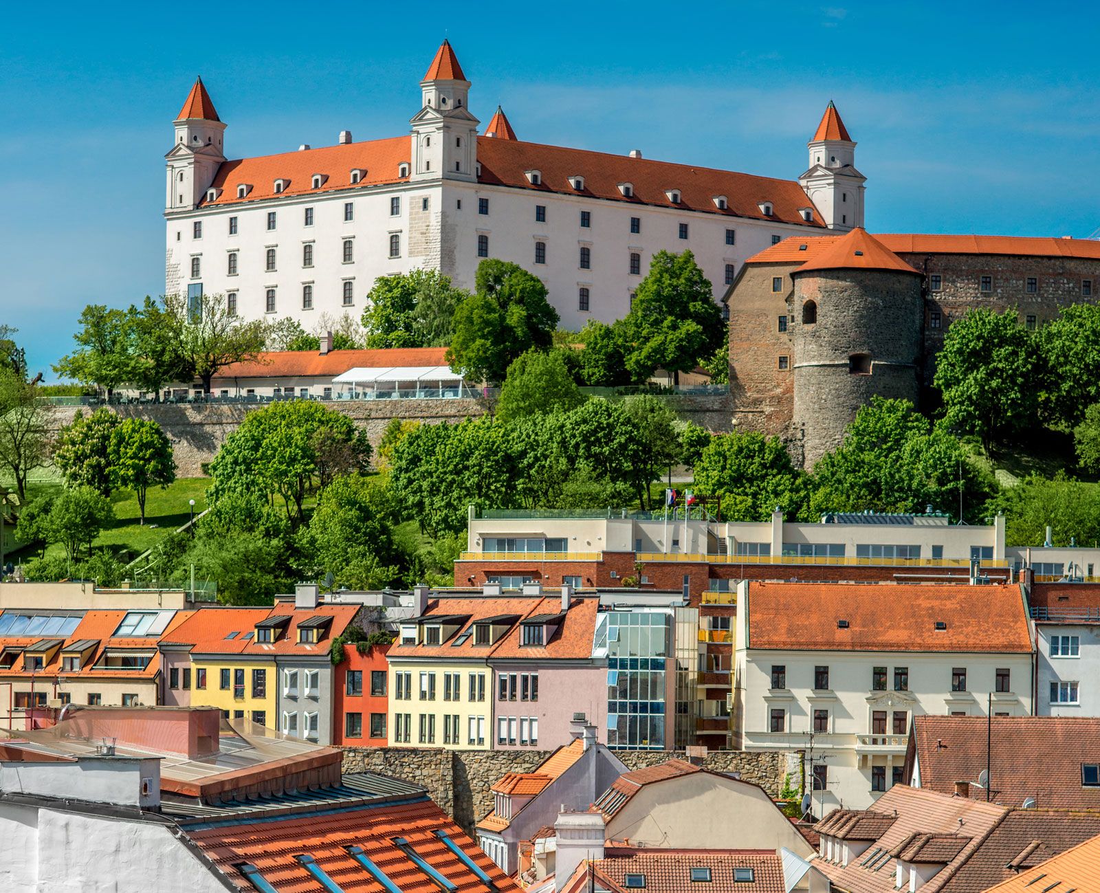 Bratislavský hrad nad farebnými historickými domami na slnečnom dni, zachytený v meste Bratislava, Slovensko.