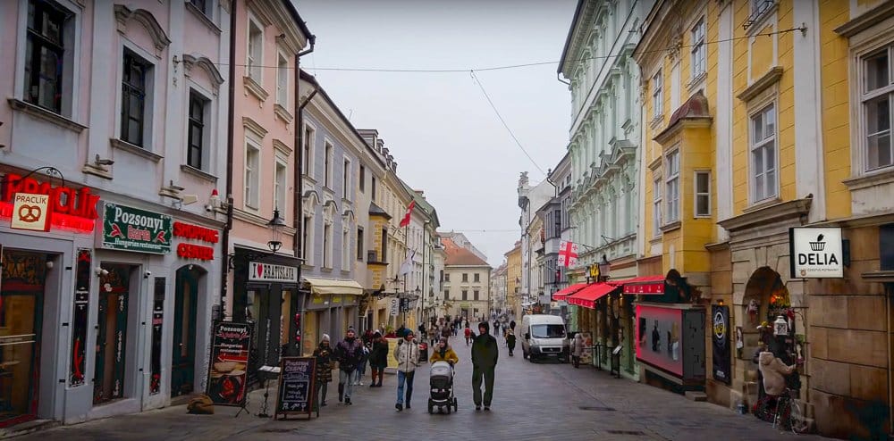 Historická ulica v centre Bratislavy s obchodmi a pešími turistami počas dňa.