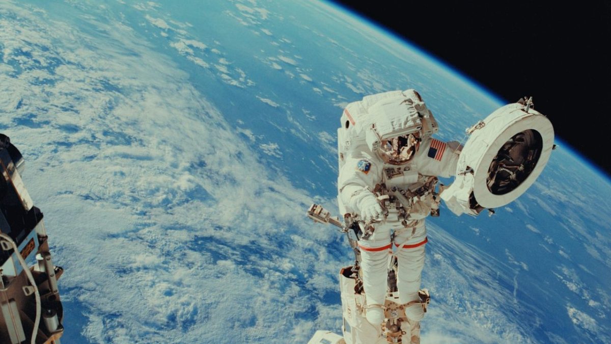 Astronaut opravuje vesmírnu stanicu na obežnej dráhe Zeme, pohľad na modrú zemeguľu v pozadí.