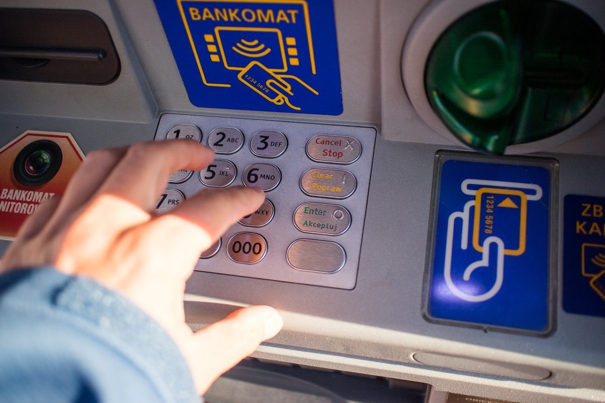 Osoba zadávajúca PIN kód na bankomate, detail klávesnice a ruky.