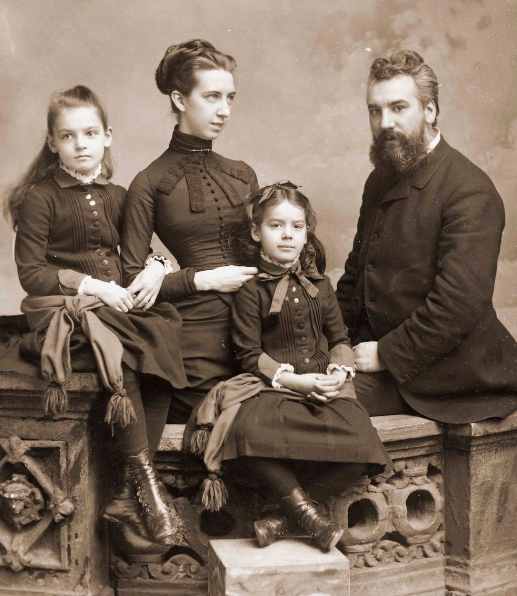Historická rodinná fotografia štyroch osôb v elegantnom oblečení, sediacich na kamennej architektúre.