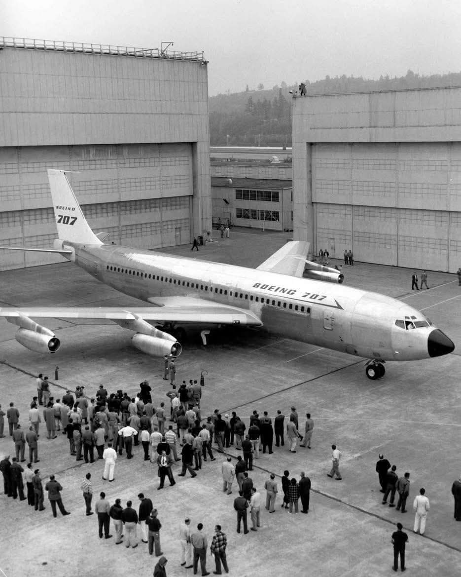 Historická fotografia Boeingu 707 pred hangárom s davmi ľudí pozorujúcimi lietadlo.
