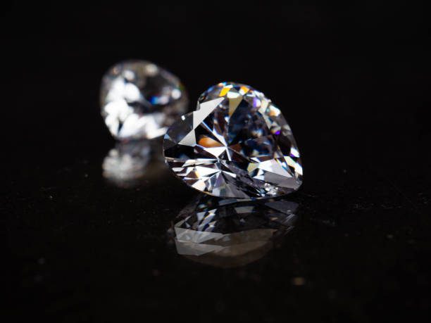 Dva ligotavé srdcové diamanty na čiernom pozadí, odrážajúce svetlo a vytvárajúce farebné odlesky.