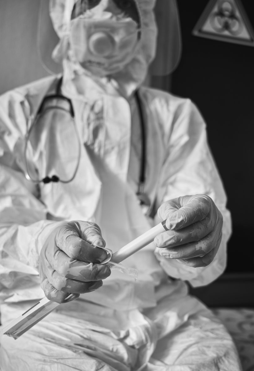 Zdravotník v ochrannom obleku pripravuje testovaciu vzorku na laboratórne vyšetrenie, čiernobiela fotografia.