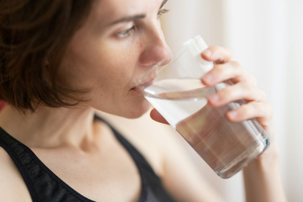 Žena pije vodu z pohára, detailný záber, zameranie na hydratáciu a zdravý životný štýl.