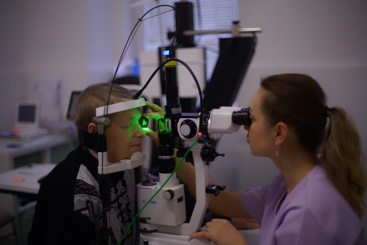 Žena vykonáva vyšetrenie očí na staršej osobe pomocou špeciálneho optického prístroja v ordinácii.