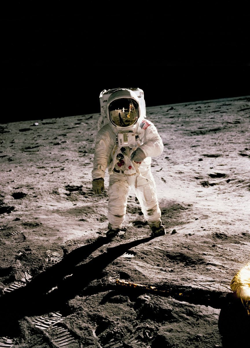 Astronaut na mesačnom povrchu v skafandri s odrazom Zeme v prilbe. História vesmírneho prieskumu.