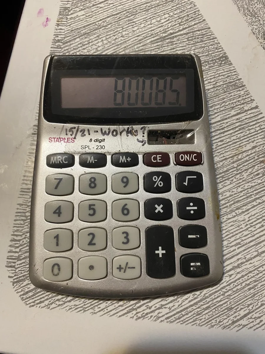 Kalkulačka zobrazuje číslicu 80085 na displeji, položená na stole s perom napísaným textom vedľa.