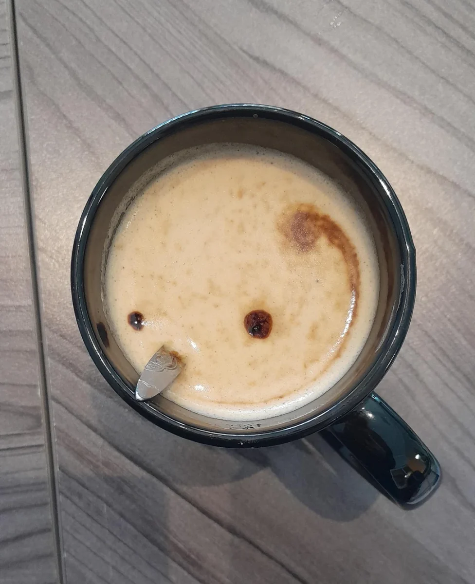 Šálka cappuccina na drevenom stole, pena s usmiatou tvárou.
