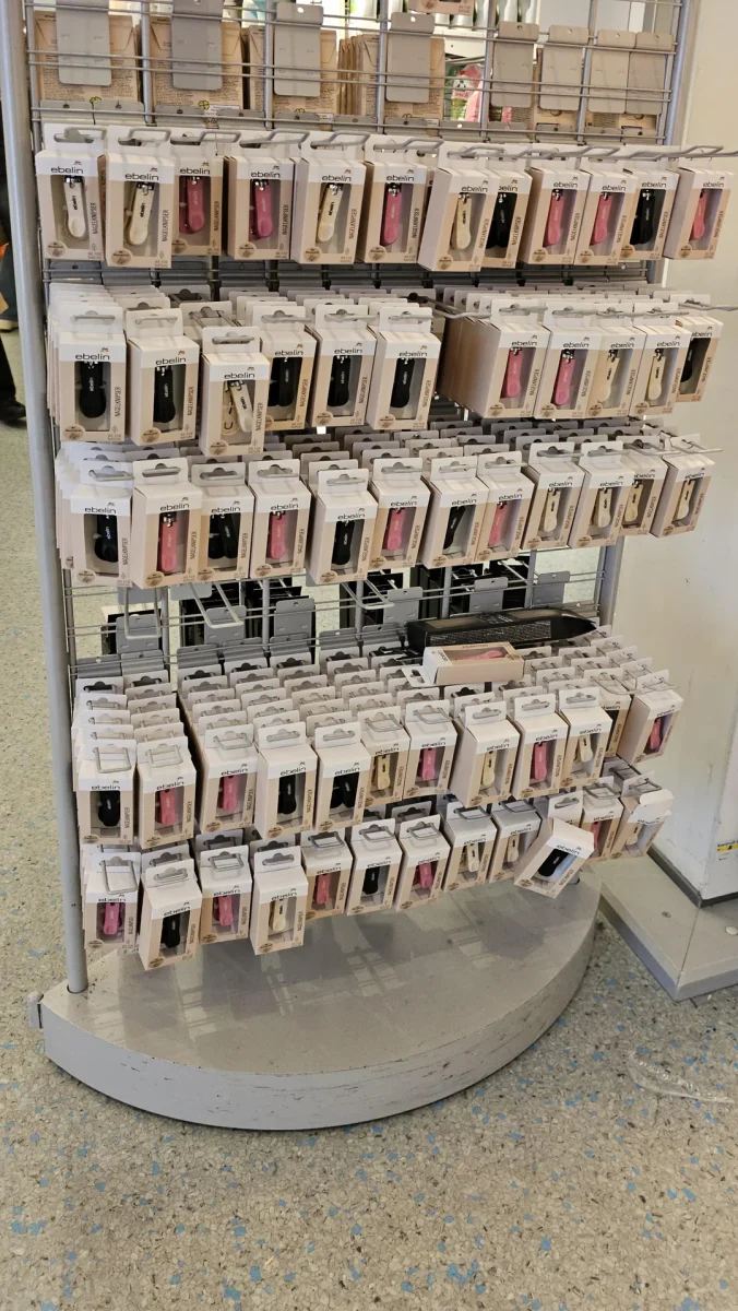 Stojan s kozmetickými produktmi v obchode, balenia klieštikov na nechty rôznych farieb a značiek.