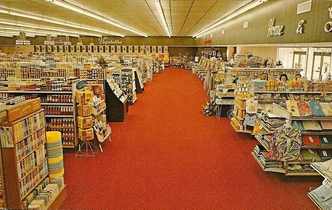 Retro interiér supermarketu s červeným kobercom a regálmi plnými tovaru.
