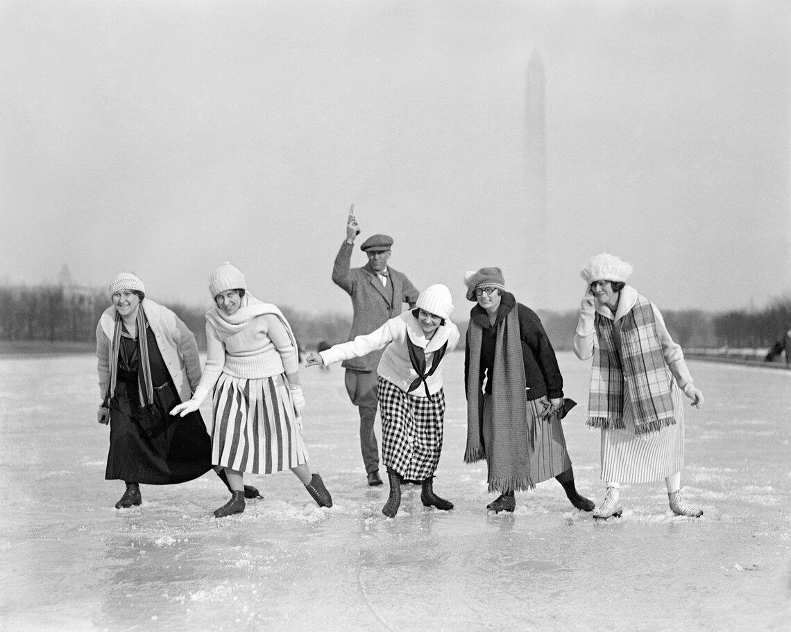 Skupina piatich žien a muža na korčuľovaní na zamrznutom jazere, 20. roky 20. storočia, Washington Monument v pozadí.
