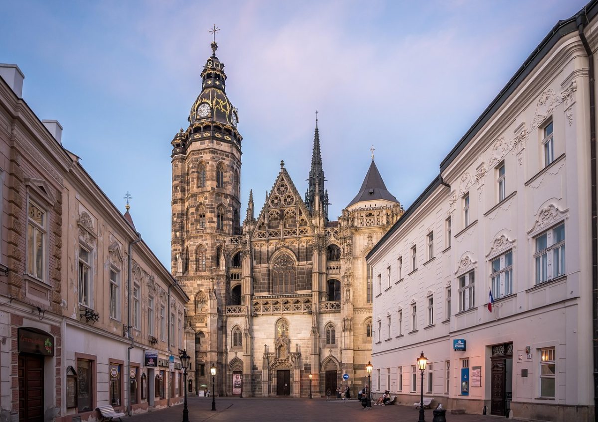 Katedrála s historickou architektúrou obklopená mestskými budovami za súmraku.