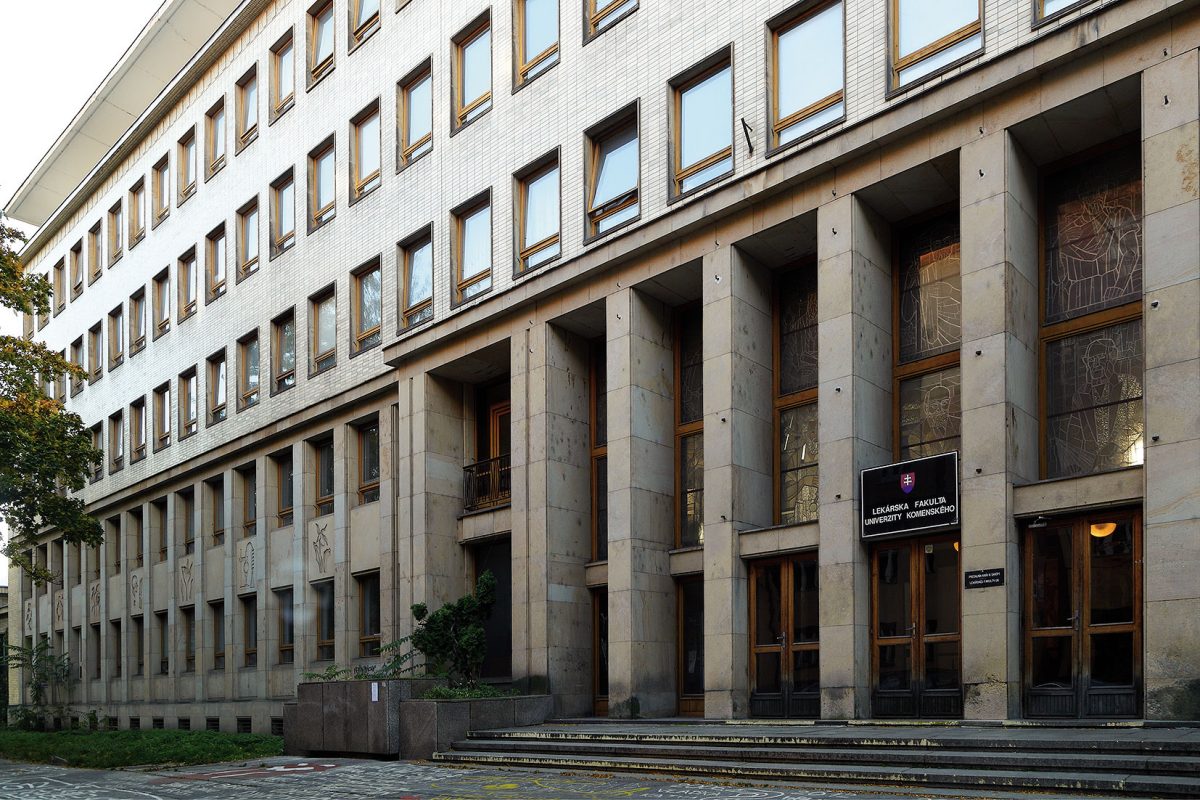 Budova v Bratislave s veľkými oknami a modernou architektúrou, stromy a kamenné schody pred vchodom.