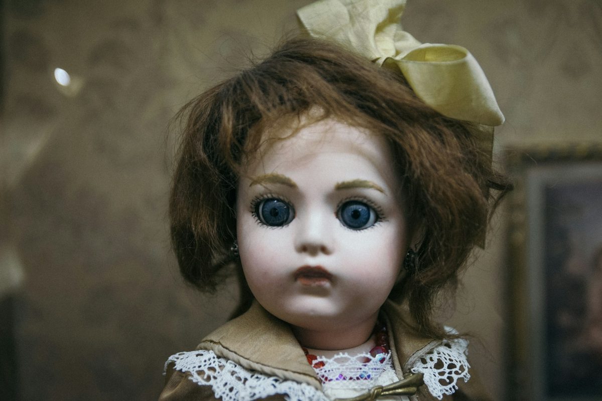 Porcelánová bábika s modrými očami a čipkovaným oblečením na vintage pozadí.