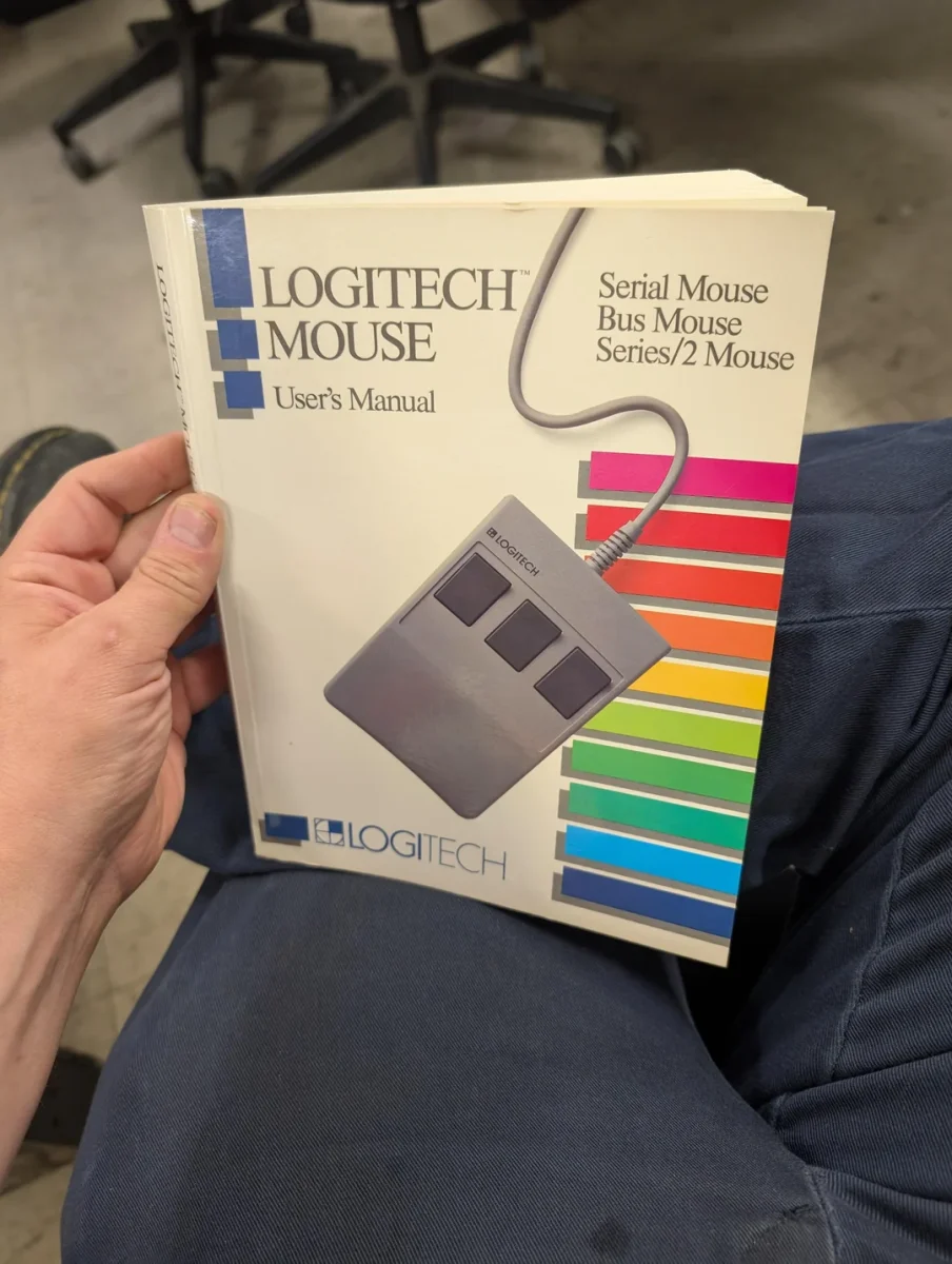 Používateľ drží manuál k myši Logitech s farebnými pruhmi a nápisom Serial Mouse Bus Mouse Series/2 Mouse.