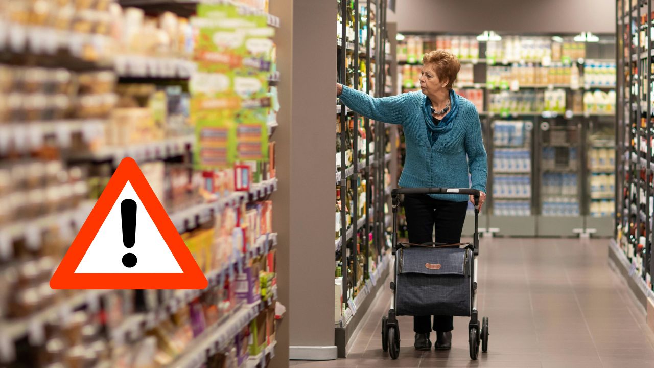 Staršia žena nakupuje v supermarkete s nákupnou taškou na kolieskach, varovný znak vedľa nej.
