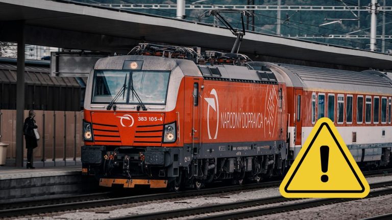Červený vlak na stanici s varovným symbolom, ktorý upozorňuje na dôležité oznámenie alebo zmenu v doprave.