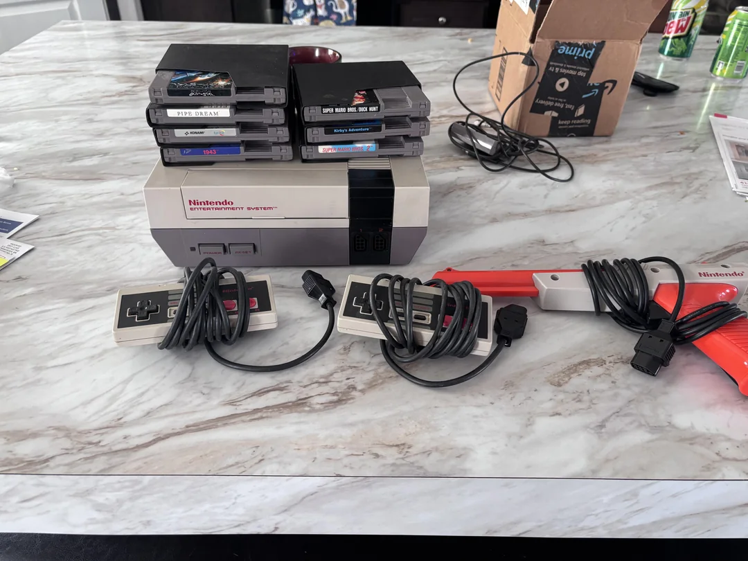 Starý Nintendo systém s hrami, ovládačmi a lightgunom na mramorovom stole, ideálny pre retro herný zážitok.