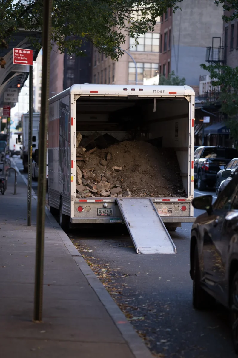 Nákladné auto s otvoreným zadným priestorom plné stavebného odpadu na mestskej ulici s rozkladanou rampou.