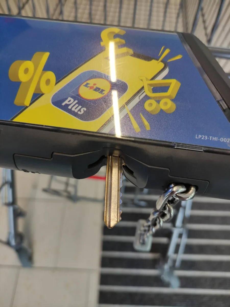 Kľúč v nákupnom vozíku s reklamou na aplikáciu Lidl Plus na pozadí.