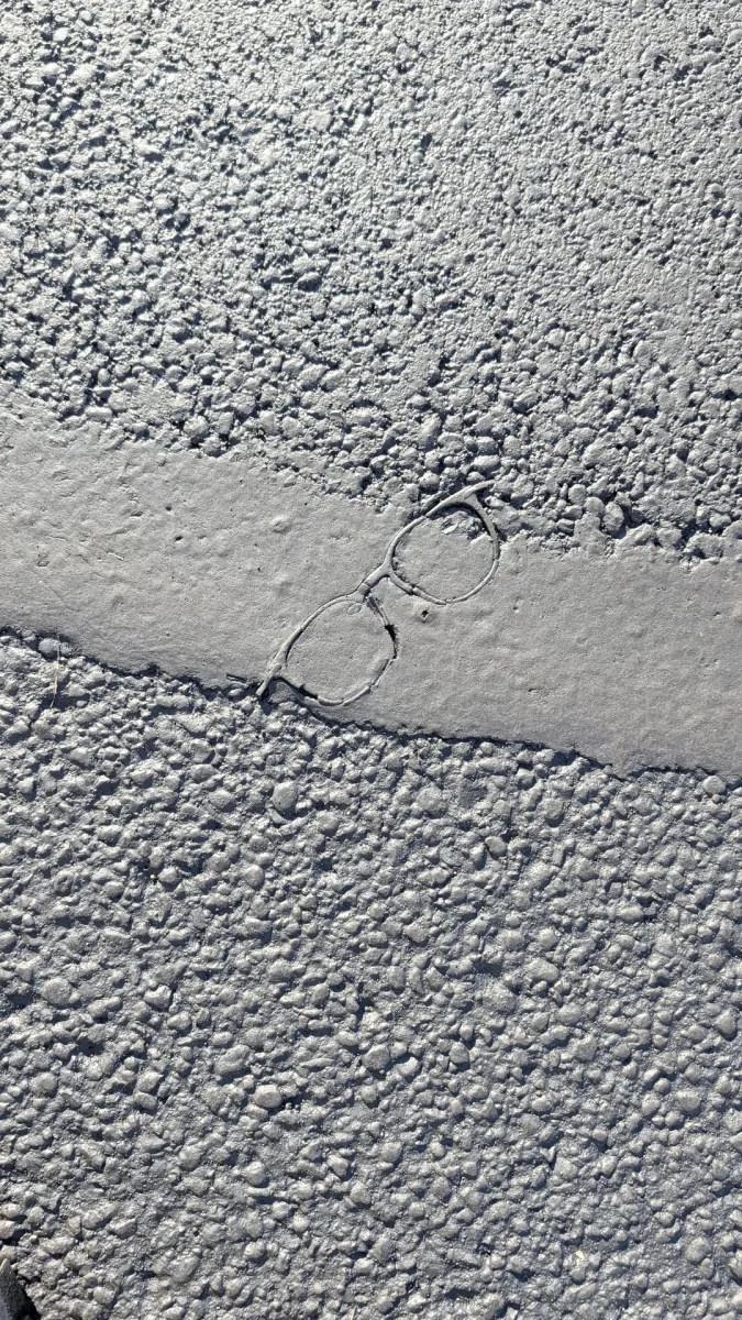 Okuliare vtlačené do čerstvého betónu na chodníku, detailný pohľad na štruktúru povrchu a otlačok.