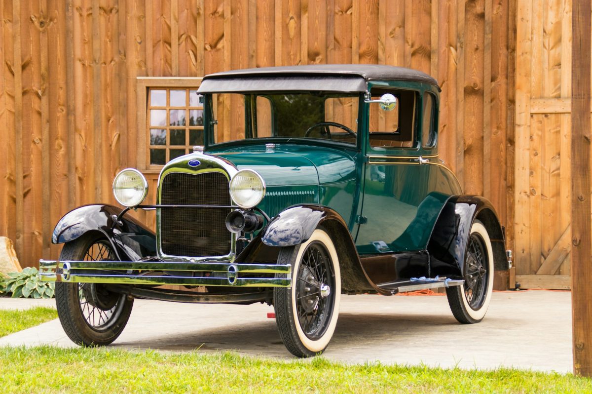 Zelené vintage auto pred drevenou stenou, historické vozidlo zo začiatku 20. storočia.