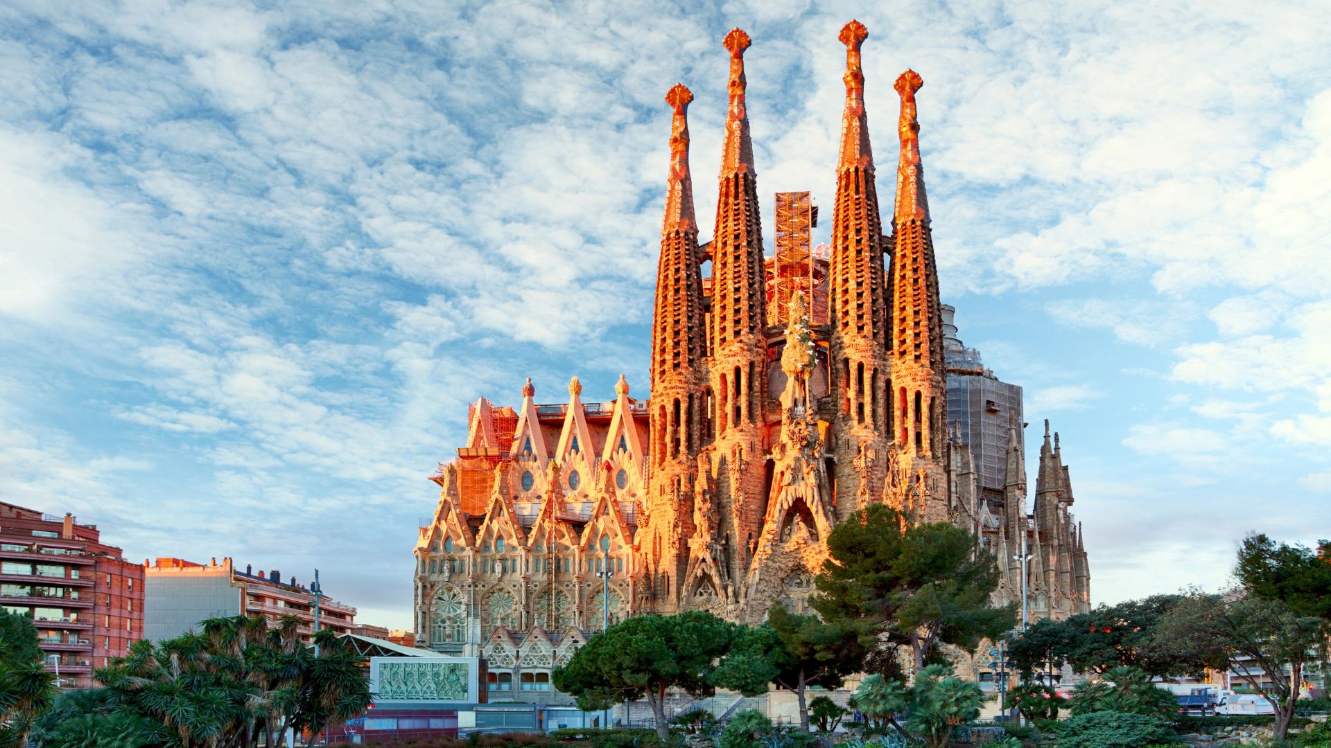 Ikonická bazilika Sagrada Familia v Barcelone za slnečného dňa, v pozadí modrá obloha s oblakmi.