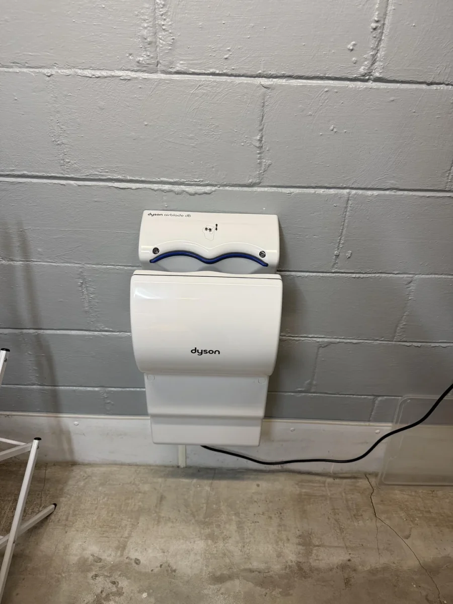 Elektrický vysúšač rúk Dyson Airblade upevnený na stene v priemyselnej miestnosti.