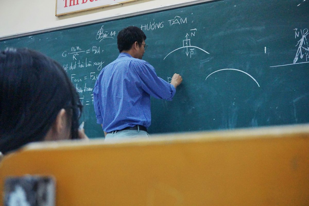 Učiteľ píše matematické vzorce na tabuľu počas hodiny, žiaci sledujú a učia sa.
