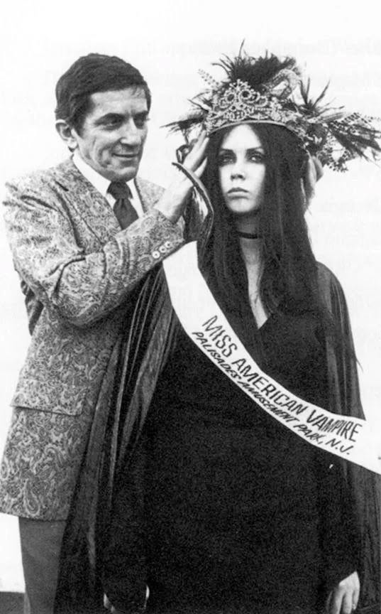 Osoba korunuje ženu vo výnimočnom kostýme s nápisom Miss American Vampire.