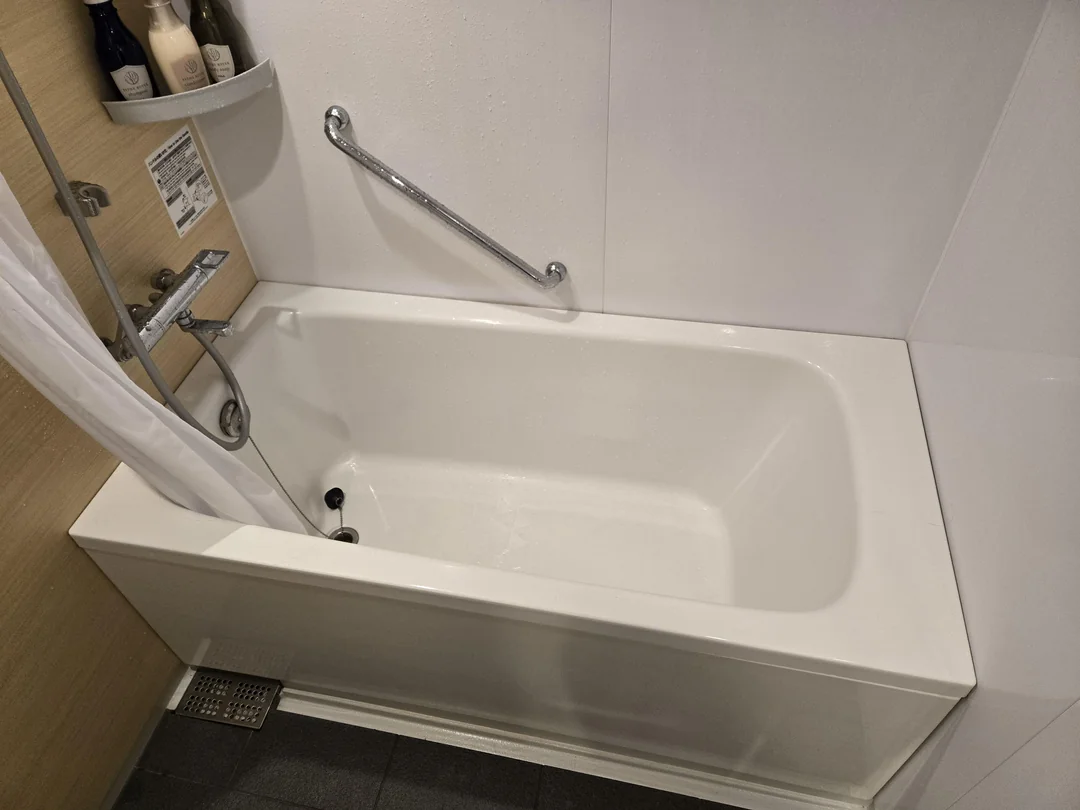 Moderná biela vaňa s chrómovou sprchou a držiakom v kúpeľni, obklopená elegantným dreveným dekorom.