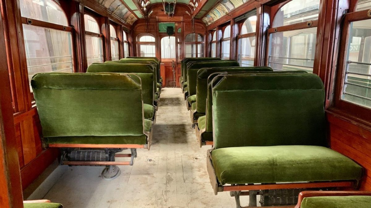 Interiér historického vlakového vozu s drevenými stenami a zelenými sedadlami.
