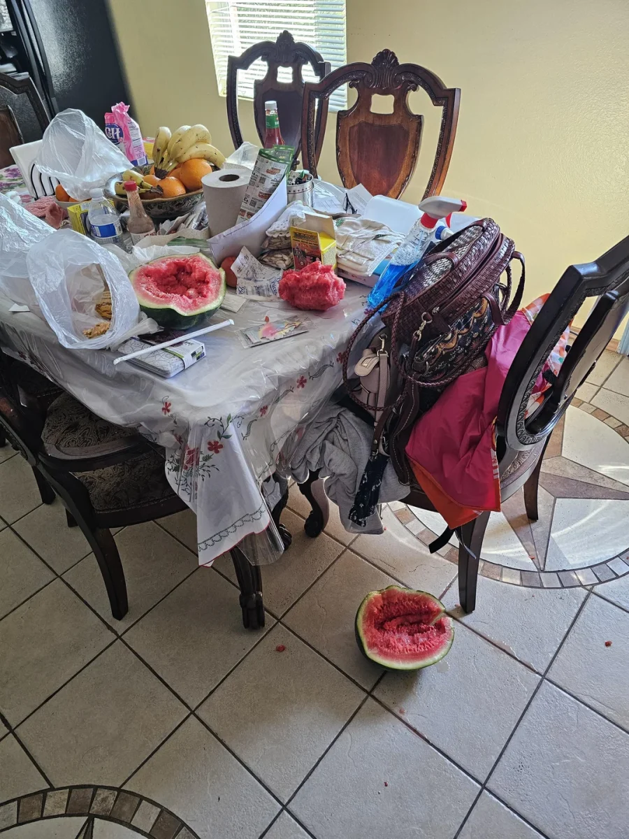 Neorganizovaný jedálenský stôl s ovocím, potravinami a rozkrojeným melónom na zemi.