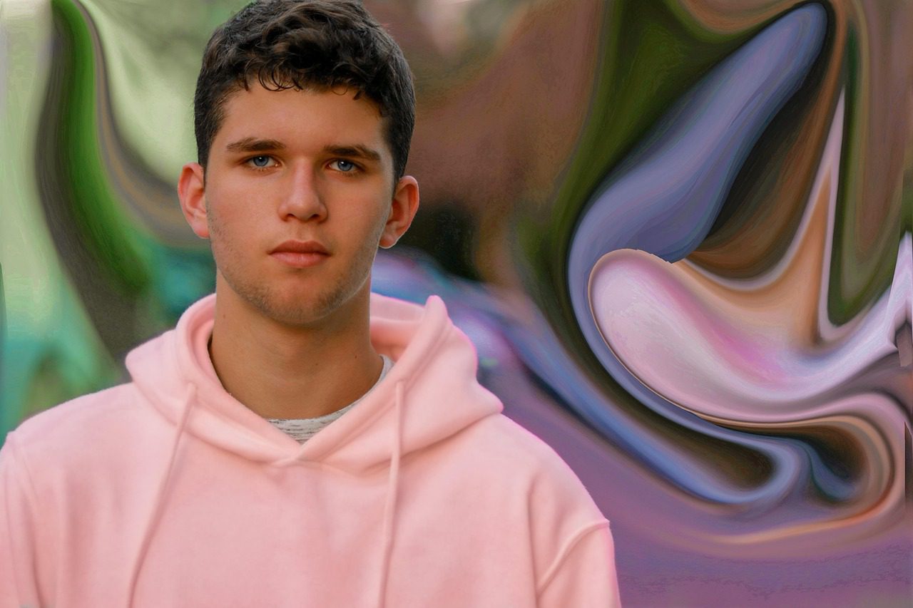 Mladý muž v ružovej mikine na abstraktnom pozadí s rozmazanými farbami.