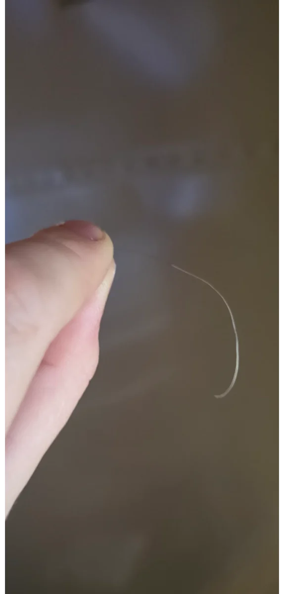 Ruka drží tenké biele vlákno pred rozmazaným pozadím.