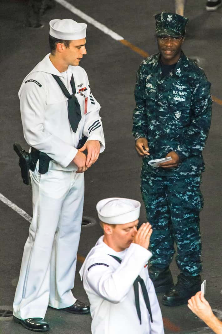 Námorníci v uniformách diskutujú a salutujú na palube lode, symbolizujú poriadok a disciplínu.