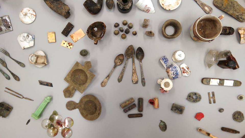Zbierka starožitných predmetov vrátane príborov, porcelánu a iných artefaktov na svetlom pozadí.