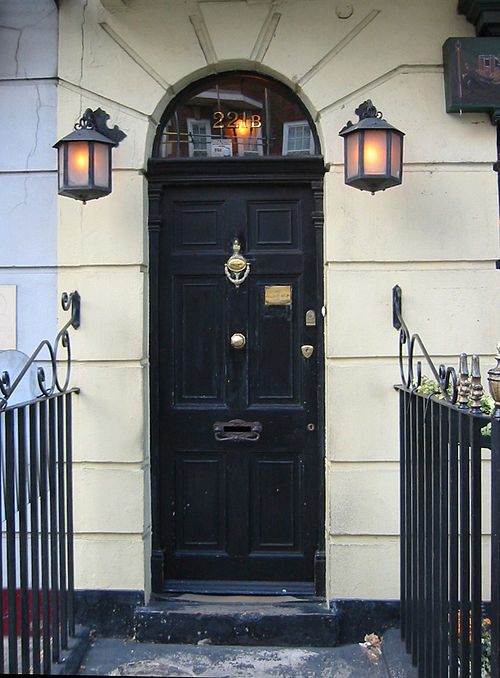 Klasické čierne dvere domu so svetlami, adresa 221B, elegantné kovové zábradlie.
