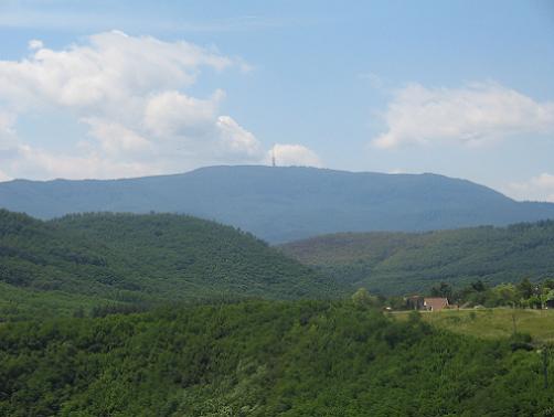 Krásna zelená krajina s výhľadom na vrch a vežu v pozadí pod modrou oblohou.