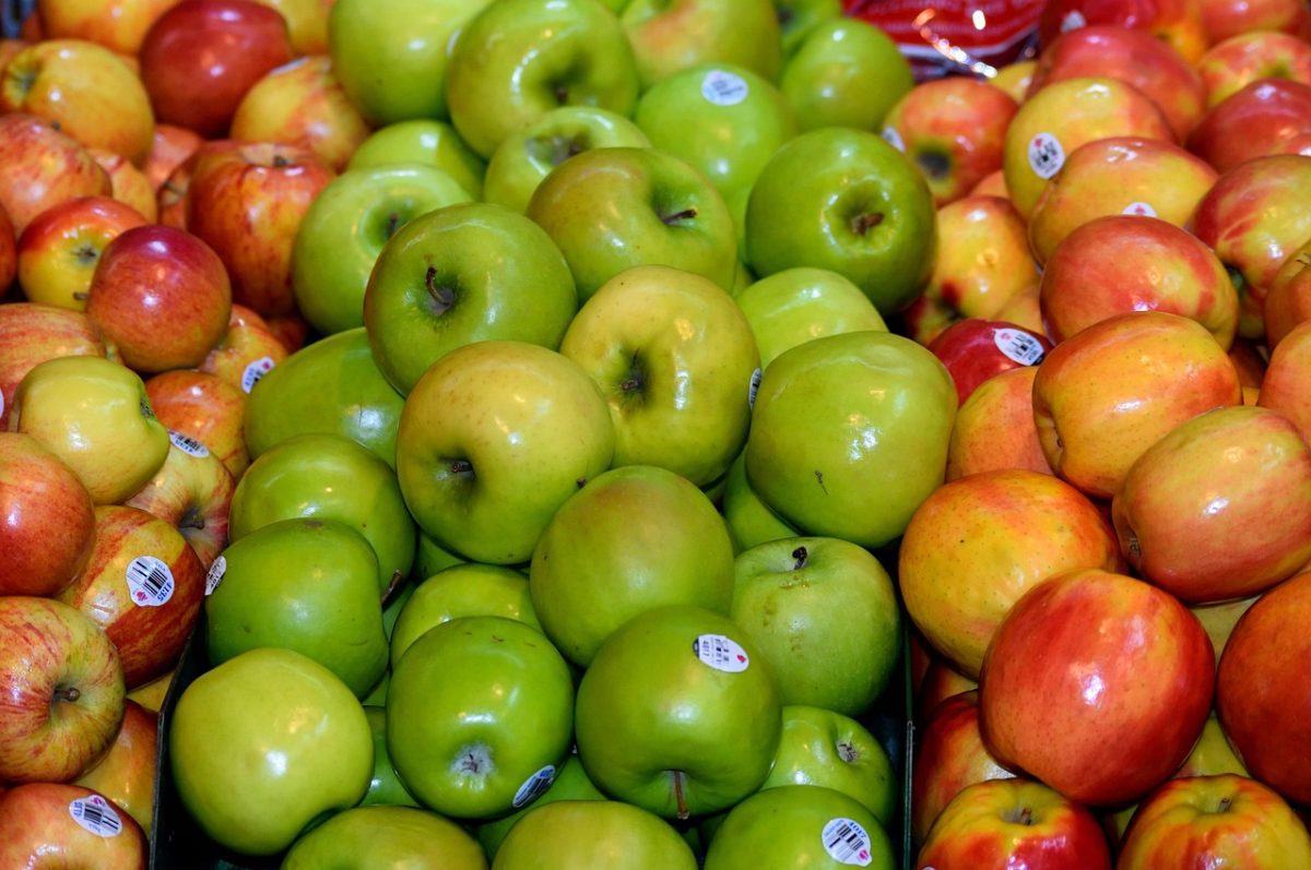 Rôzne odrody jabĺk na predaj v supermarkete, zelené a červené jablká pohromade na pultoch.