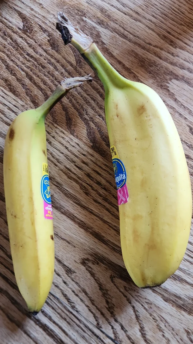 Dva banány s nálepkami na drevenom stole, jeden dlhší a druhý kratší.