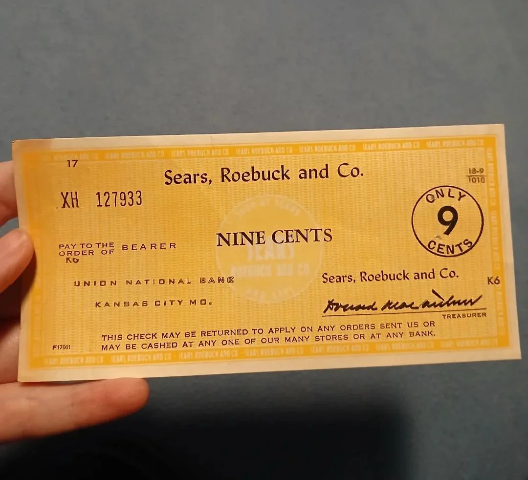 Stará šeková poukážka od Sears, Roebuck and Co. na deväť centov, držaná v ruke.