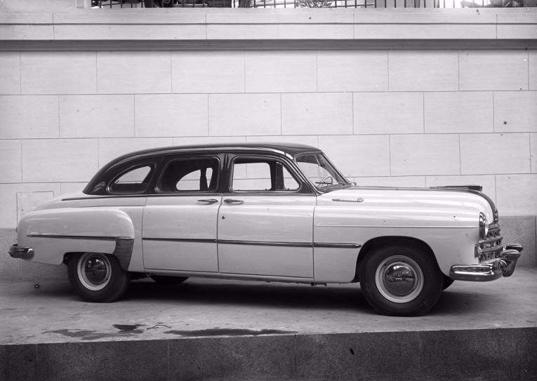 Klasické retro auto v historickej čierno-bielej fotografii pred kamennou stenou.