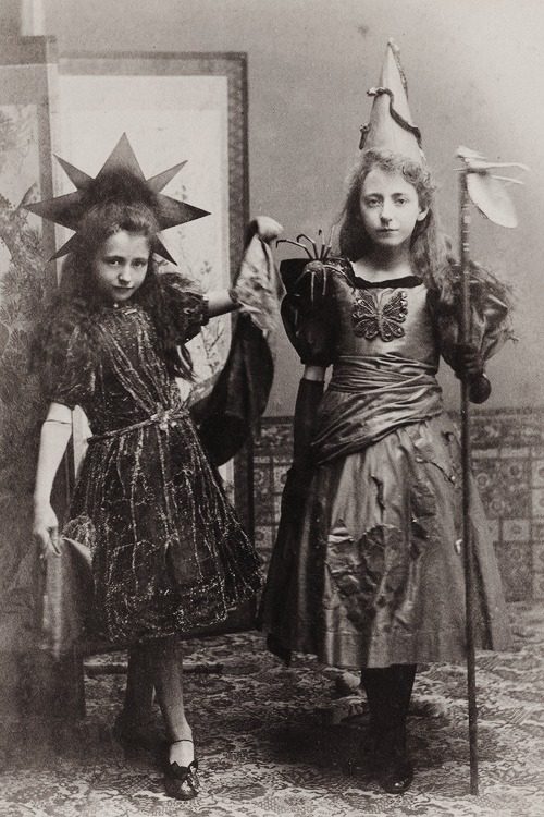 Deti v historických kostýmoch s klobúkmi a palicou, vintage fotografia v interiéri.