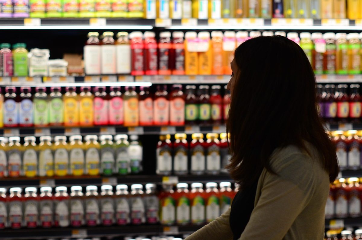 Žena nakupuje nápoje v supermarkete, stojí pred regálom s rôznymi fľašami.