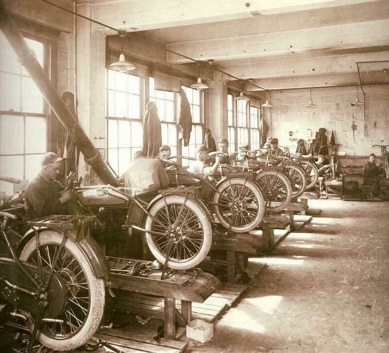 Dielňa na výrobu motocyklov, robotníci montujú motocykle pri oknách v historickom závode.