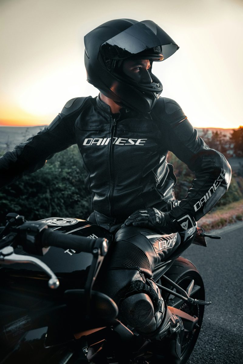 Motorkár v koženej kombinéze na motorke pri západe slnka, pripravený na jazdu.